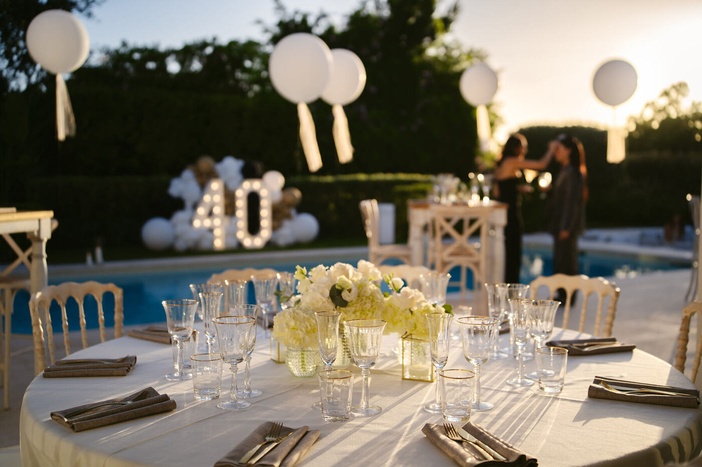 Poolside tablescape with gold-rimmed glassware and white florals at golden hour