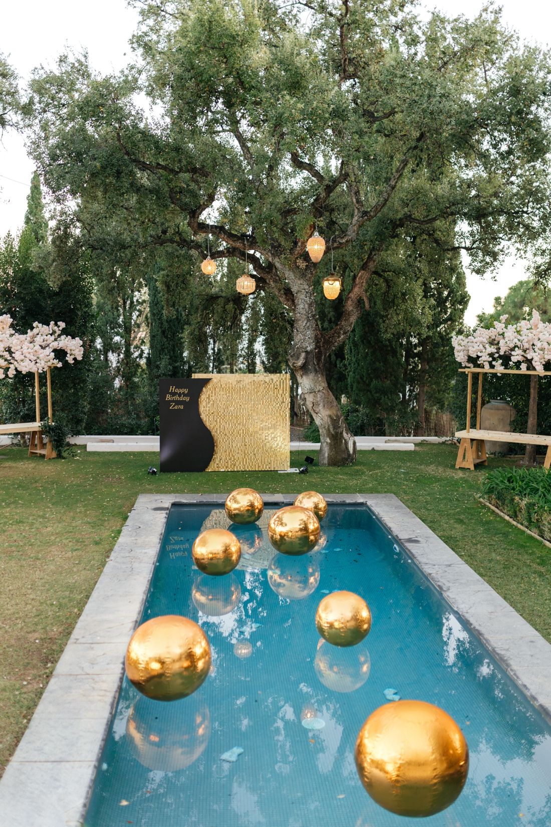 Gold mirror orbs floating in a pool beneath an olive tree, Marbella