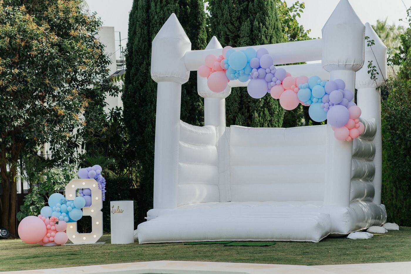 White bouncy castle with pastel balloon garland and marquee number, Marbella birthday